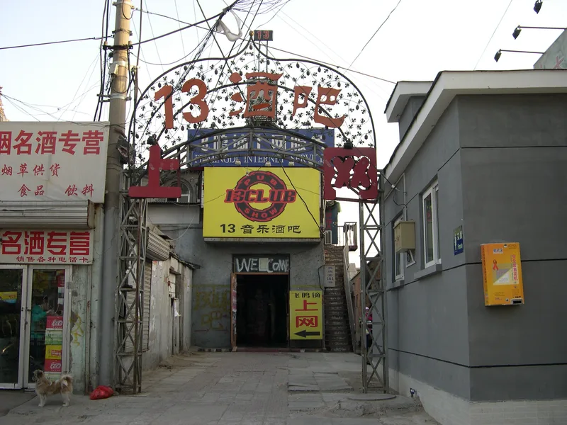 The entrance arch of 13 Club in Beijing with its red neon sign and a narrow alley behind