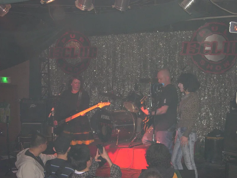 Kang Mao of SUBS singing on stage with JEF at 13 Club, the crowd's raised hands and cameras in front