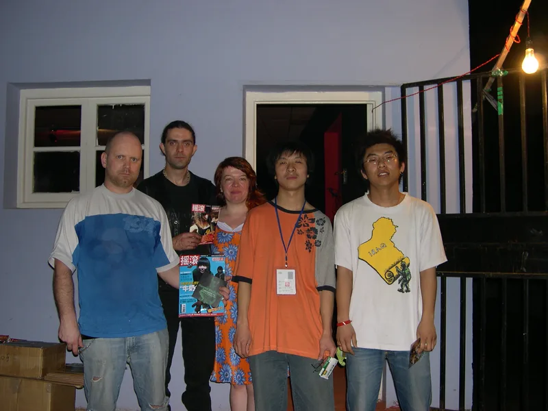 Kjell, Pez and Katy with two young Chinese hosts outside a pale blue building at night, holding Chinese rock magazines