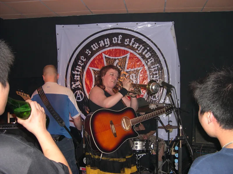 Katy playing trumpet and Kjell on guitar in front of a large 4698 banner with an iron cross logo