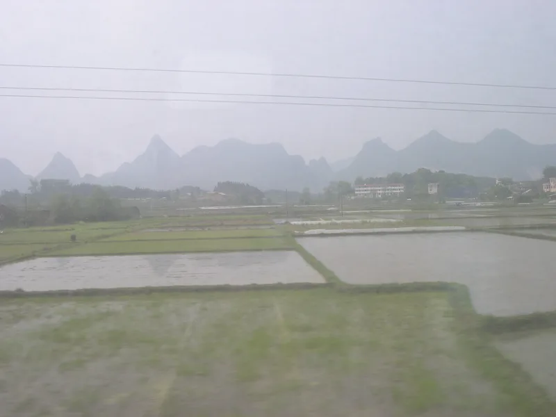 Flooded rice paddies and a line of karst hills in mist, seen from a moving train