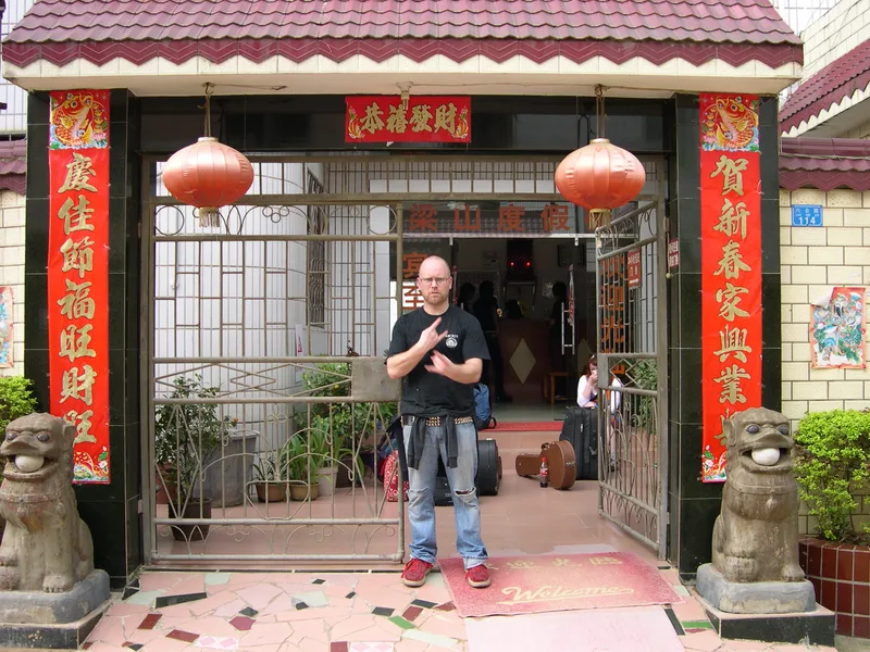 Kjell standing in the gateway of a guesthouse in Guilin with red lanterns, red banners and the band's luggage around him
