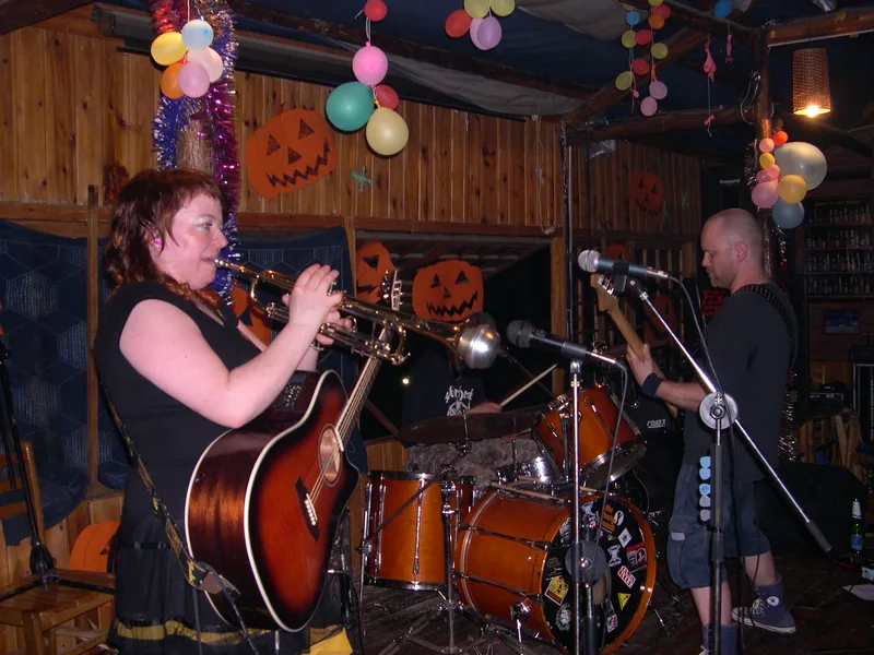 Katy on trumpet and Kjell on guitar on a small wooden stage decorated with paper pumpkins and balloons at Shuanle Bar