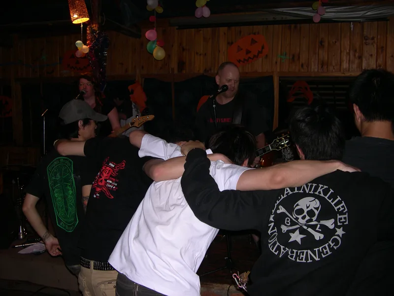 A row of young people with arms around each other's shoulders facing the stage at Shuanle Bar