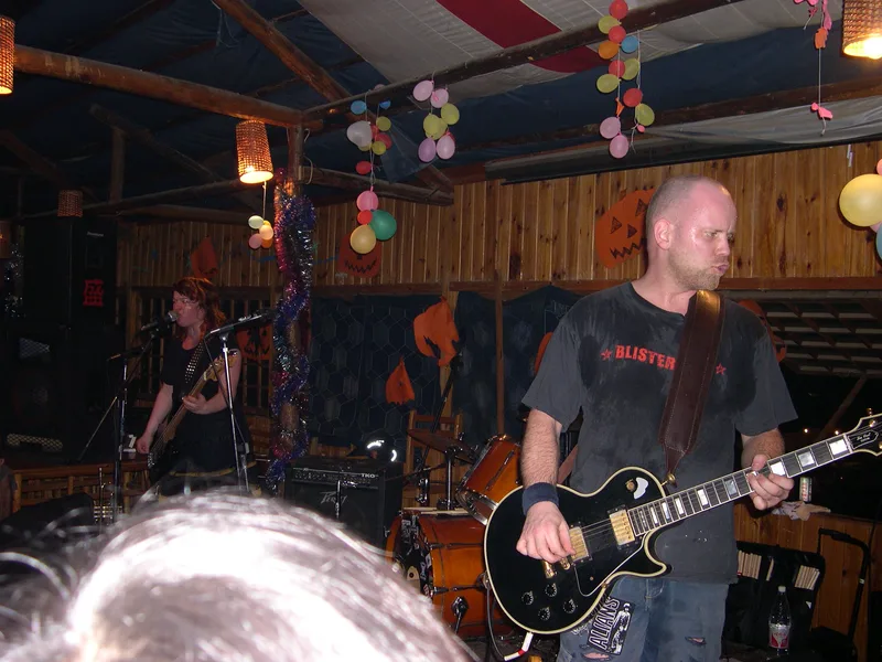 Katy on bass and Kjell on guitar at Shuanle Bar, Pez on drums behind a kit with stickers