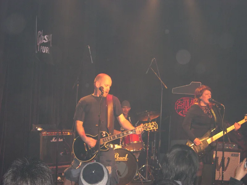 Kjell and Katy playing at Yuyintang in Shanghai, a Gibson logo on the black wall behind them and the crowd's heads in front