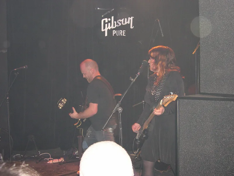 Kjell on guitar and Katy on bass close together under the Gibson Pure sign at Yuyintang