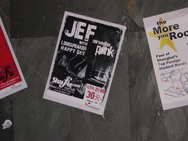 A wall of gig posters including a JEF China tour poster with the band's photo