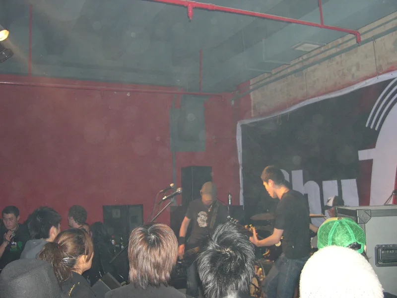 JEF on the Shufle stage seen over a crowd of heads, the Shufle banner filling the wall behind the band