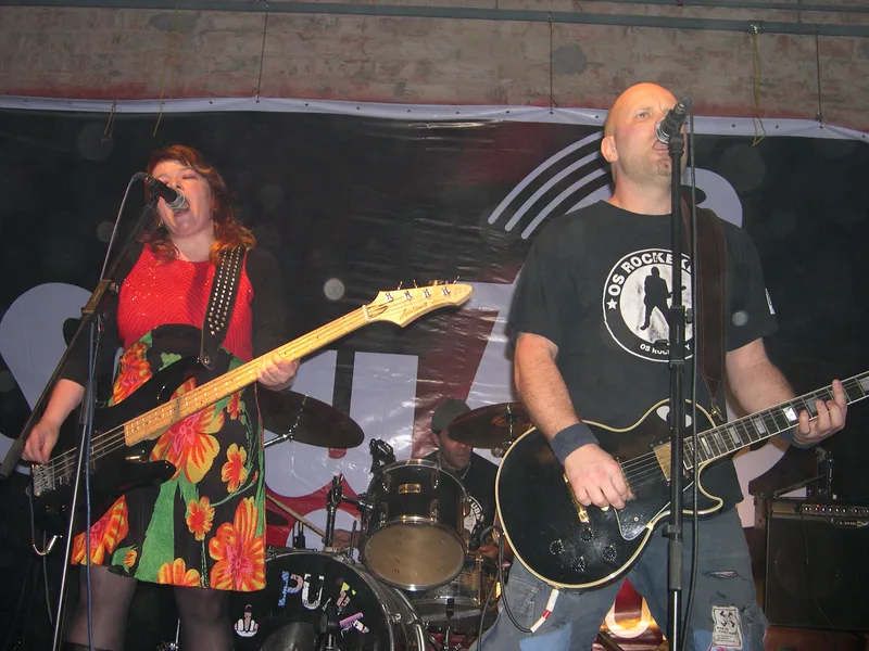 Katy singing at the microphone with her bass and Kjell on guitar under the Shufle banner